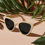 Beige cat-eye sunglasses on peach background with tropical leaves
