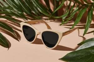 Beige cat-eye sunglasses on peach background with tropical leaves