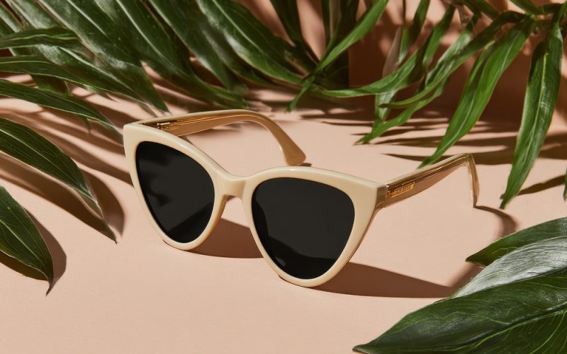 Beige cat-eye sunglasses on peach background with tropical leaves